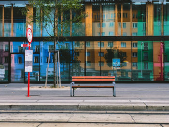 Empty bench by street against buildings in city