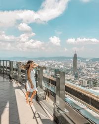 Side view of woman standing on balcony in city against sky