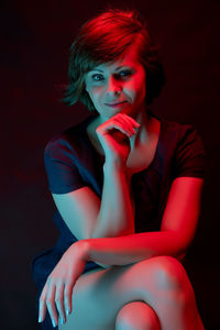 Portrait of smiling woman sitting against black background