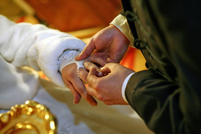 Midsection of groom putting ring in bride finger