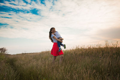 Girl carrying brother on field against sky