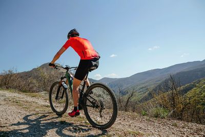 Man on bicycle riding mountain trail in background blue sky and mountains