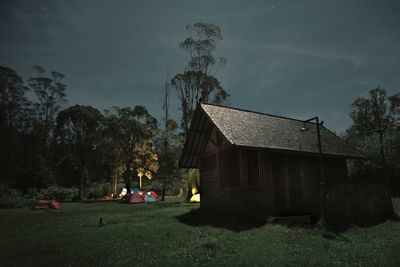 People sitting on field by building against sky at night