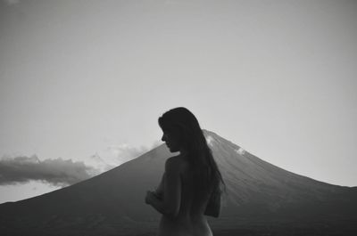 Rear view of shirtless woman standing against mountain and sky during dusk