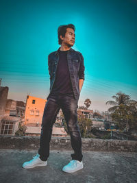 Young man looking away while standing against blue sky