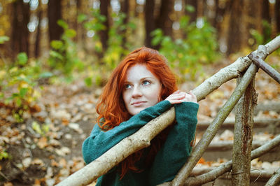 Portrait of happy redhead woman with arms raised in forest