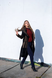 Full length portrait of woman standing against wall