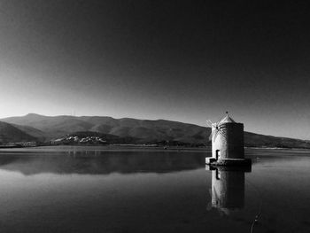 Traditional windmill by lake against clear sky