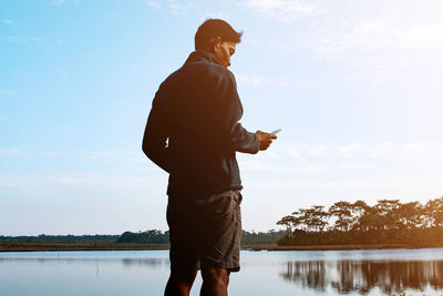 Man using mobile phone while standing in lake against sky