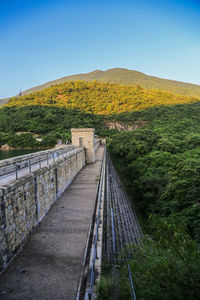 Bridge leading towards mountains against clear sky