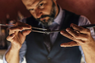 Midsection of mature bartender holding fruit with serving tongs in bar