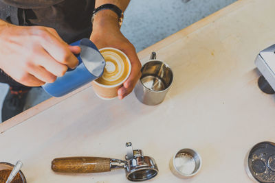 Cropped image of hand making froth art in espresso coffee at counter in cafe