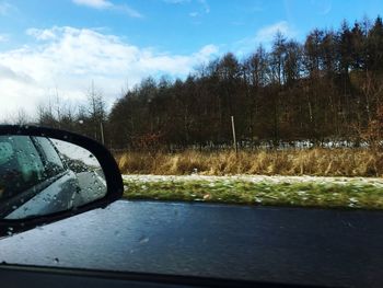 Close-up of side-view mirror by car against sky