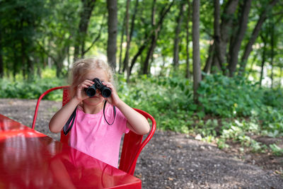 Close-up of girl looking through binoculars at table in forest