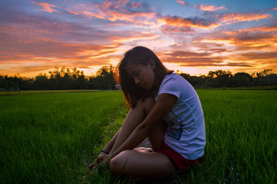 Woman sitting on field against sky during sunset