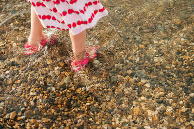 Childrens bare feet in rubber sandals stand on a pebble beach in sea water summer