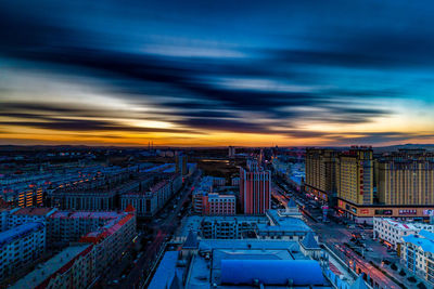 High angle view of illuminated city buildings against sky at sunset