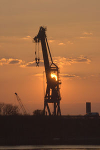 Silhouette crane at construction site against sky during sunset reflecting 