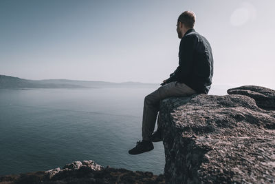 Man sitting on rock looking at mountain against sky