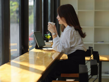 Side view of a woman drinking coffee cup on table