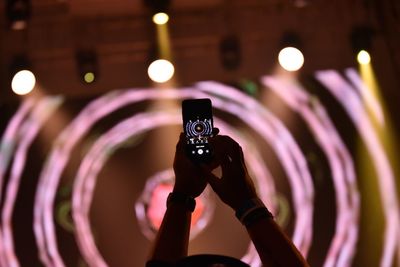 Close-up of hand photographing against illuminated lights