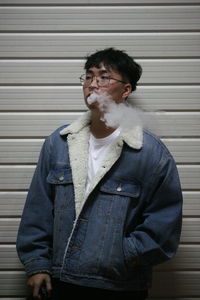 Young man wearing eyeglasses standing against wall