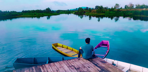 Rear view of man sitting on pier over lake