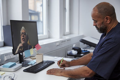 Male doctor having online consultation with senior patient