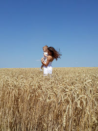 Mother carrying son while standing on grassy field against clear blue sky during sunny day