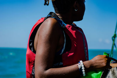 Midsection of woman by sea with a life jacket against blue sky