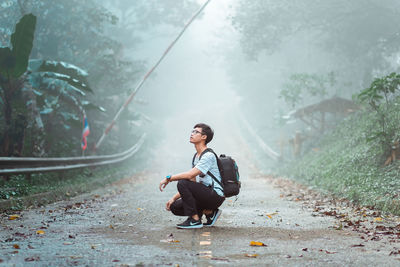 Young woman sitting on street amidst trees