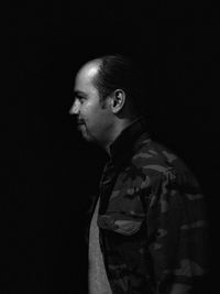 Side view of young man looking away against black background