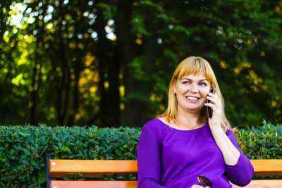 Portrait of a smiling young woman using phone outdoors