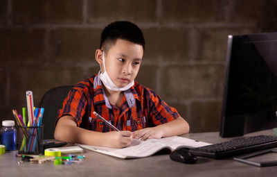 Happy boy studying with face mask on table at home