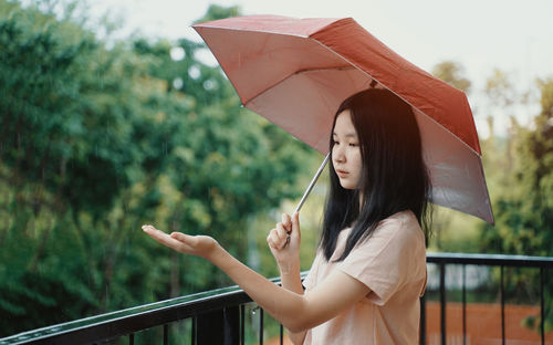 Woman holding umbrella while standing on railing during rainy season