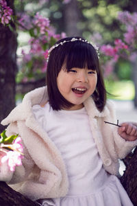 Korean girl in a white light fur coat and a headband sitting on a tree branch in a garden