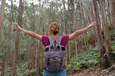 Rear view of woman with arms raised standing in forest