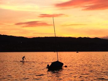 Silhouette man paddleboarding on lake zurich during sunset