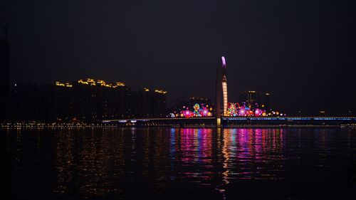 Illuminated bridge over river by buildings against sky at night