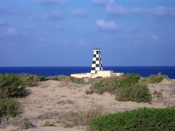 Lighthouse on beach by sea against sky