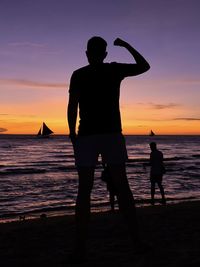 Rear view of man standing at beach against sky during sunset