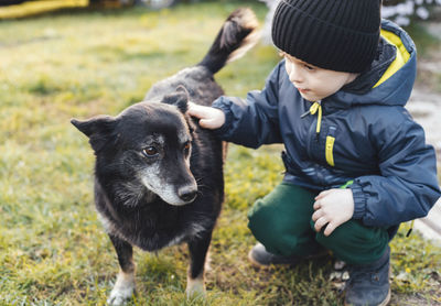 Boy squatting and petting a dog outdoors. friendship and care for animals