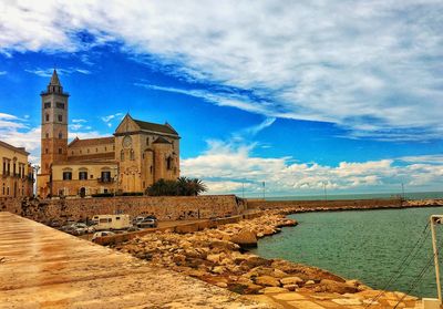 Buildings by sea against cloudy sky