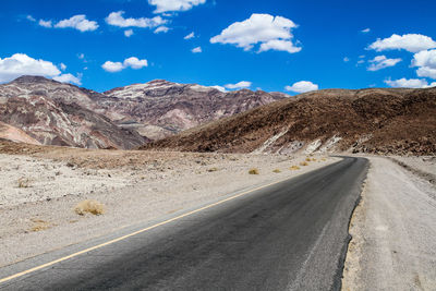 Empty road by mountains against sky