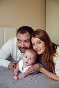 Mom and dad are lying on the bed with the baby in warm clothes