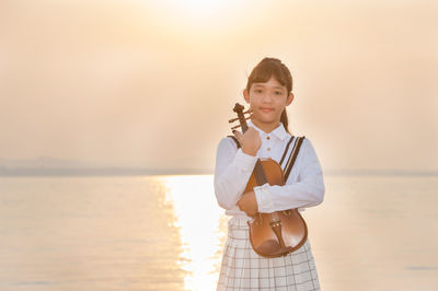 Girl with violin standing in sea against sky