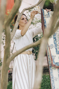 Beautiful woman hanging bed sheet for drying in garden