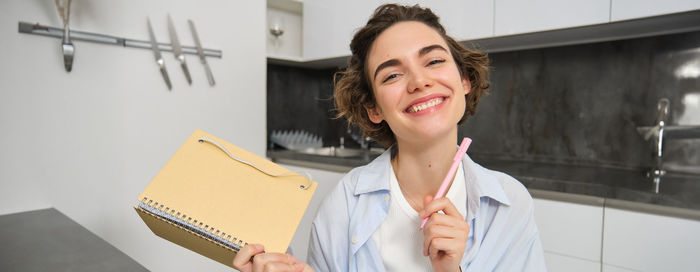 Portrait of young woman using mobile phone while standing in office