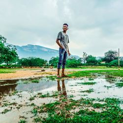 Full length of young man standing in rain against sky