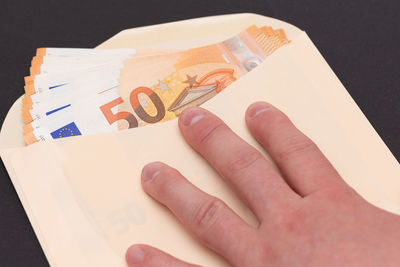 Cropped hand of person holding paper currency against black background
